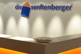 Das Logo der Senftenberg an einer weißen Wand.